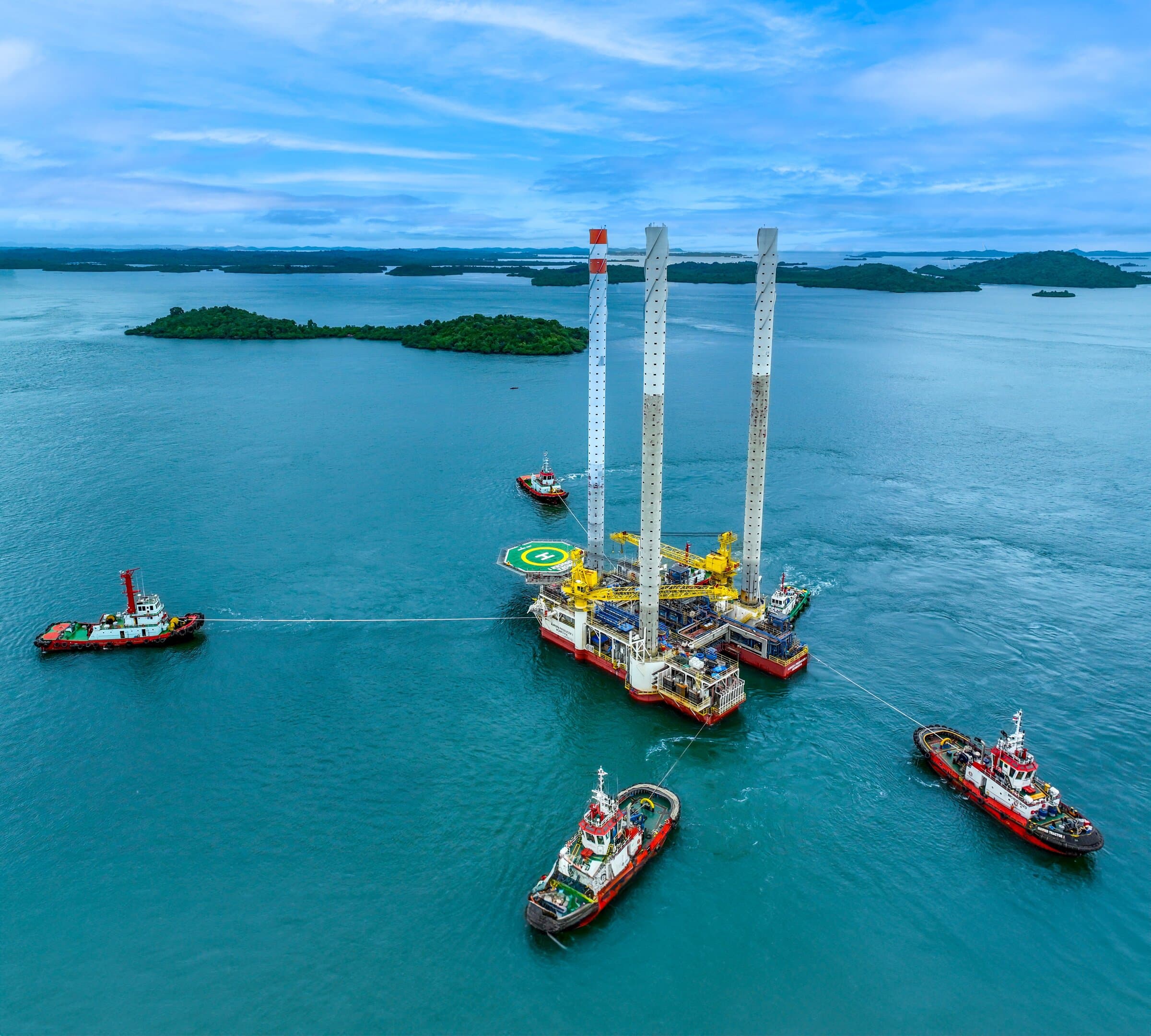 Jack-up offshore platform being positioned by tugboats in tropical waters